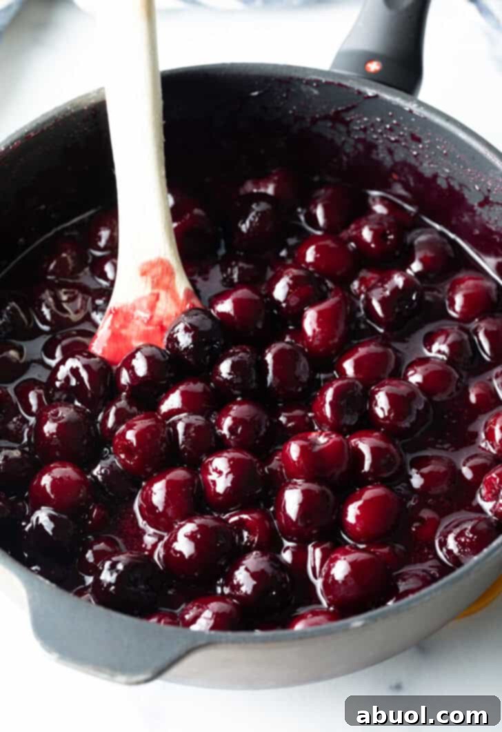 Cooking homemade cherry pie filling in a large pot, stirring with a wooden spoon.