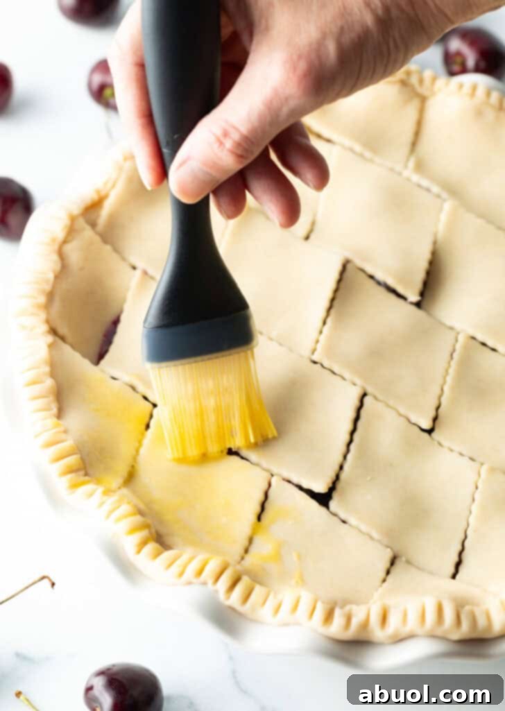 Hand brushing melted butter over the top of the unbaked pie.