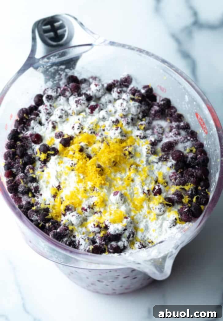 Combining blueberries, lemon zest, flour and sugar in a glass mixing bowl.