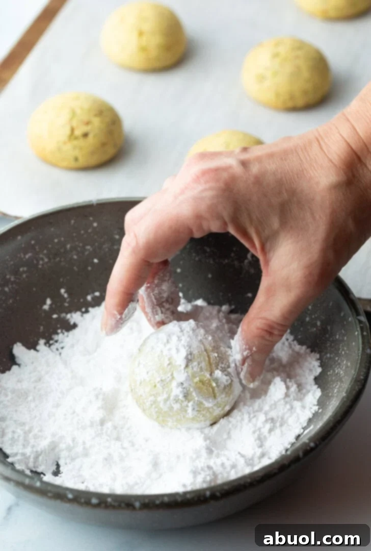 Sweet Italian Bridal Bites 9 A hand rolling a round cookie in a bowl of powdered sugar.