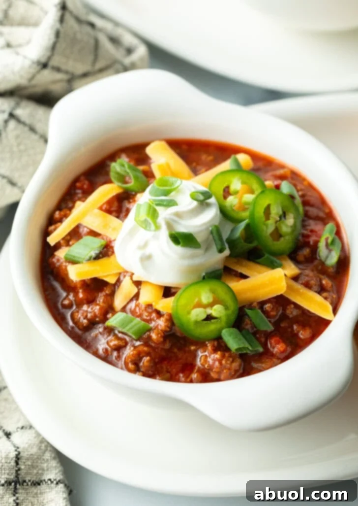 Top down view of a white bowl of beanless chili topped with shredded cheese, jalapeno slices, sour cream and chopped green onions.
