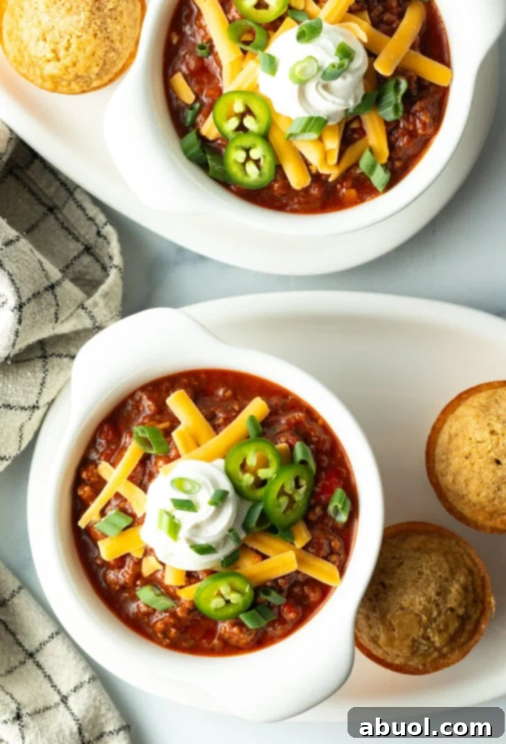 Top down view of a white bowl of beanless chili con carne topped with shredded cheese, jalapeno slices, sour cream and chopped green onions.