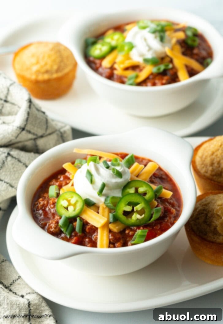 Top down view of a white bowl of beanless chili con carne topped with shredded cheese, jalapeno slices, sour cream and chopped green onions.