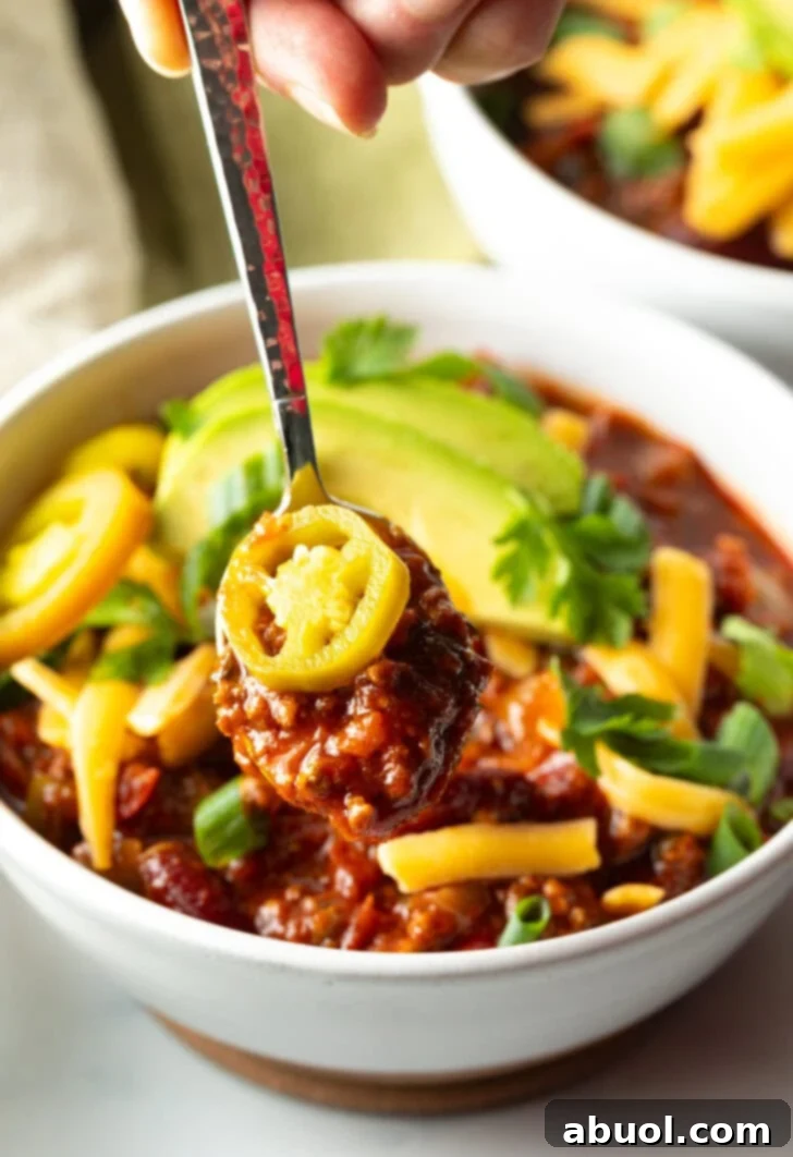 Bowl of chili with pickled jalapeno peppers, shredded cheese, slices of avocado and chopped green onions