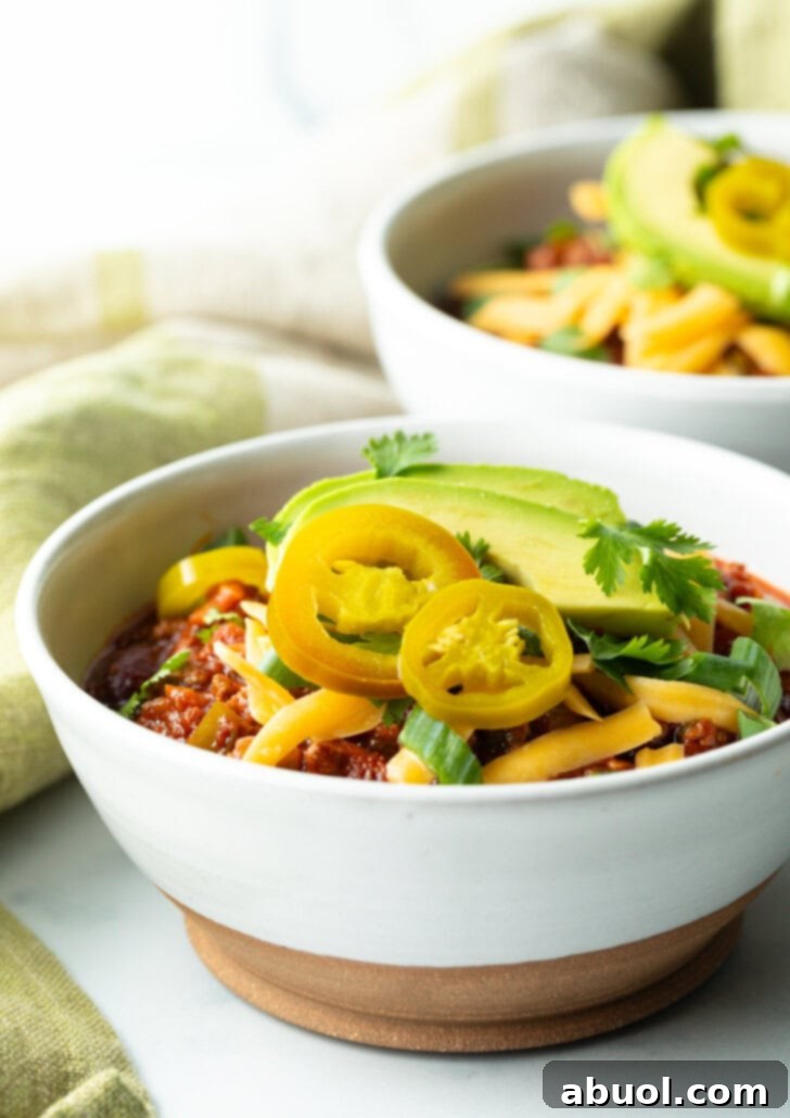 Bowl of chili with pickled jalapeno peppers, shredded cheese, slices of avocado and chopped green onions