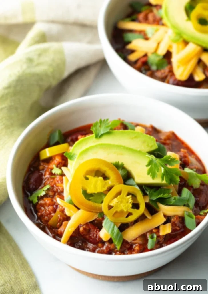 Bowl of chili with pickled jalapeno peppers, shredded cheese, slices of avocado and chopped green onions