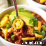 Bowl of chili with pickled jalapeno peppers, shredded cheese, slices of avocado and chopped green onions