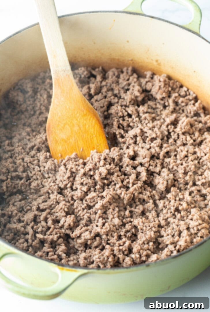 Browning ground venison meat in a large cooking pot with a wooden spatula.