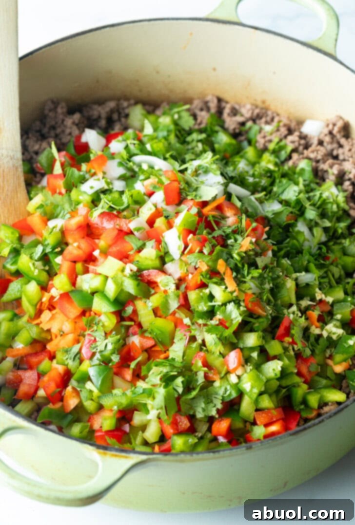 Adding chopped fresh peppers and herbs to pot of ground venision.