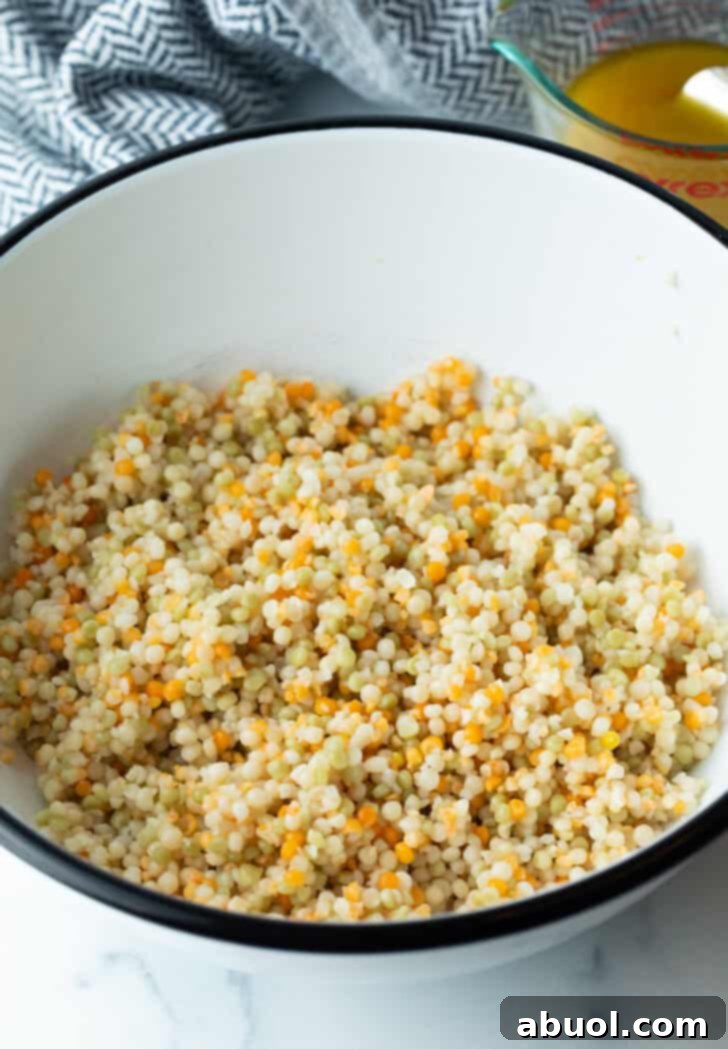 Cooked and cooled pearl couscous in a large mixing bowl, perfectly prepared as the base for the salad.