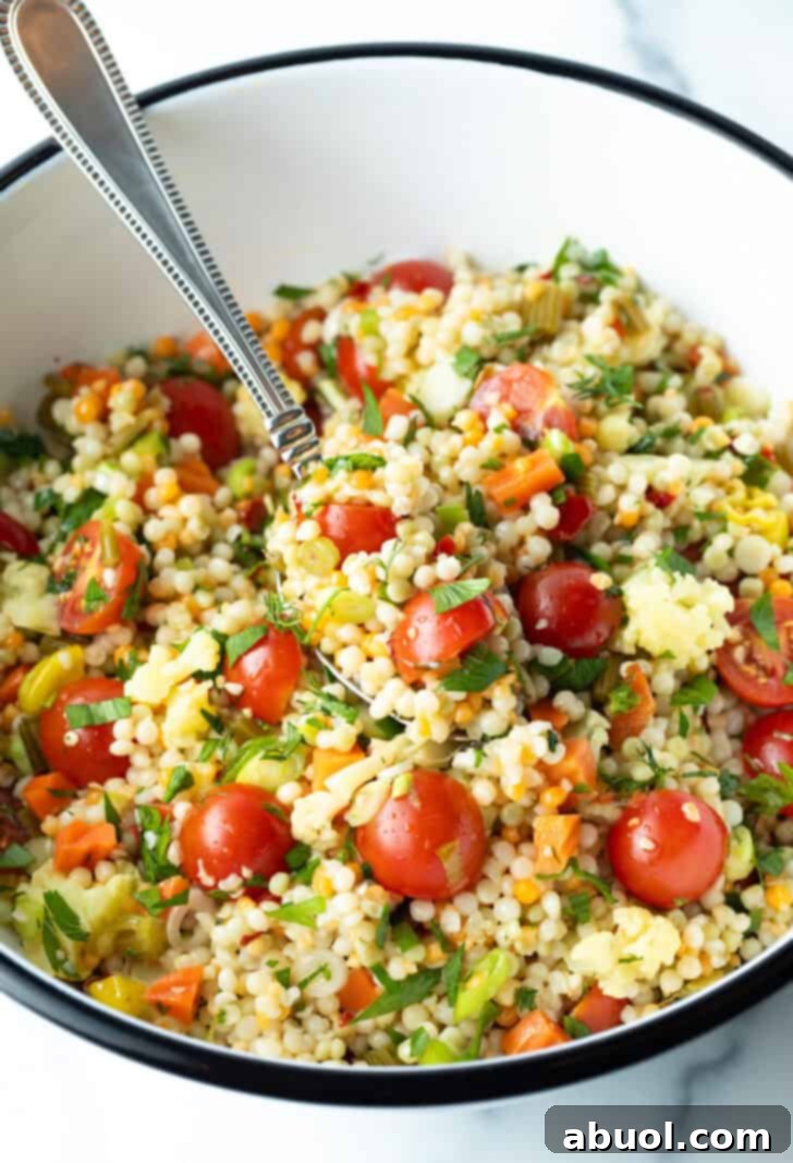 Pearl couscous salad, generously filled with chopped tomatoes, fresh herbs, and tangy pickled vegetables, presented beautifully in a large white mixing bowl.