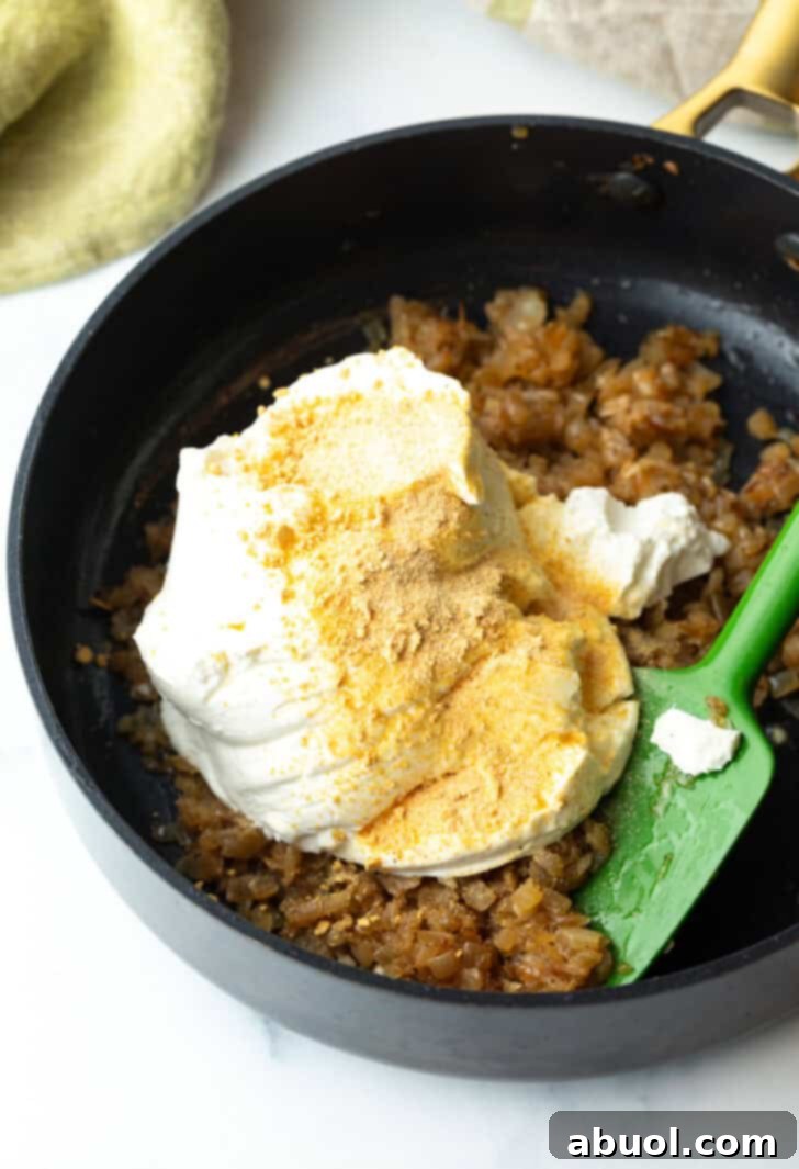 Adding cream cheese and spices to the perfectly browned and chopped caramelized onions in a large cooking pot, ready for mixing.