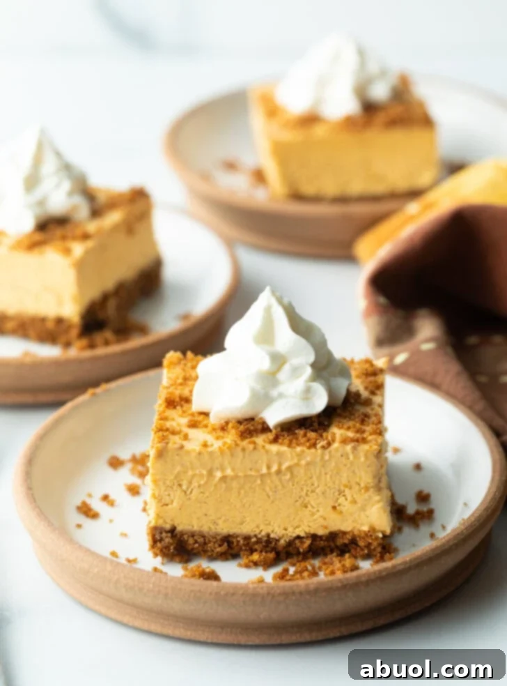 A perfectly square slice of pumpkin pie cheesecake on a white plate, elegantly topped with whipped cream.