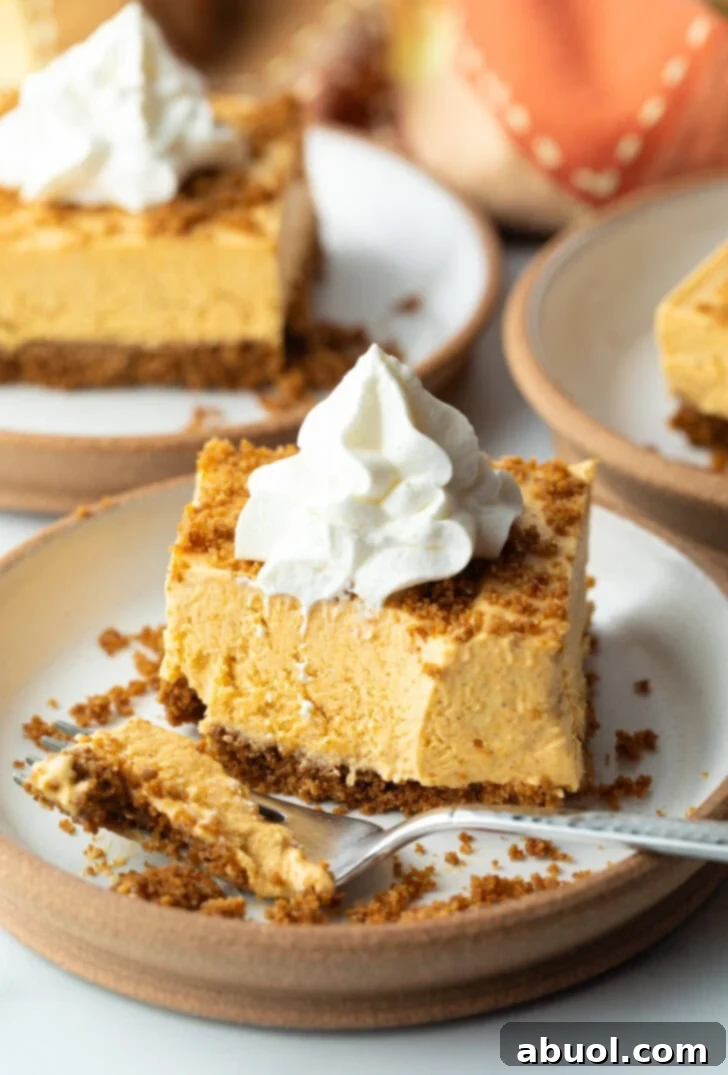 A square of pumpkin pie cheesecake on a white plate, topped with whipped cream, with a fork holding a bite of the dessert.