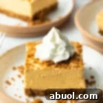 Square of pumpkin pie cheesecake on a white plate, topped with whipped cream.