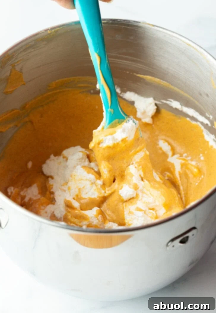 Pumpkin puree and softened cream cheese being mixed together in a large metal bowl with a blue spatula.