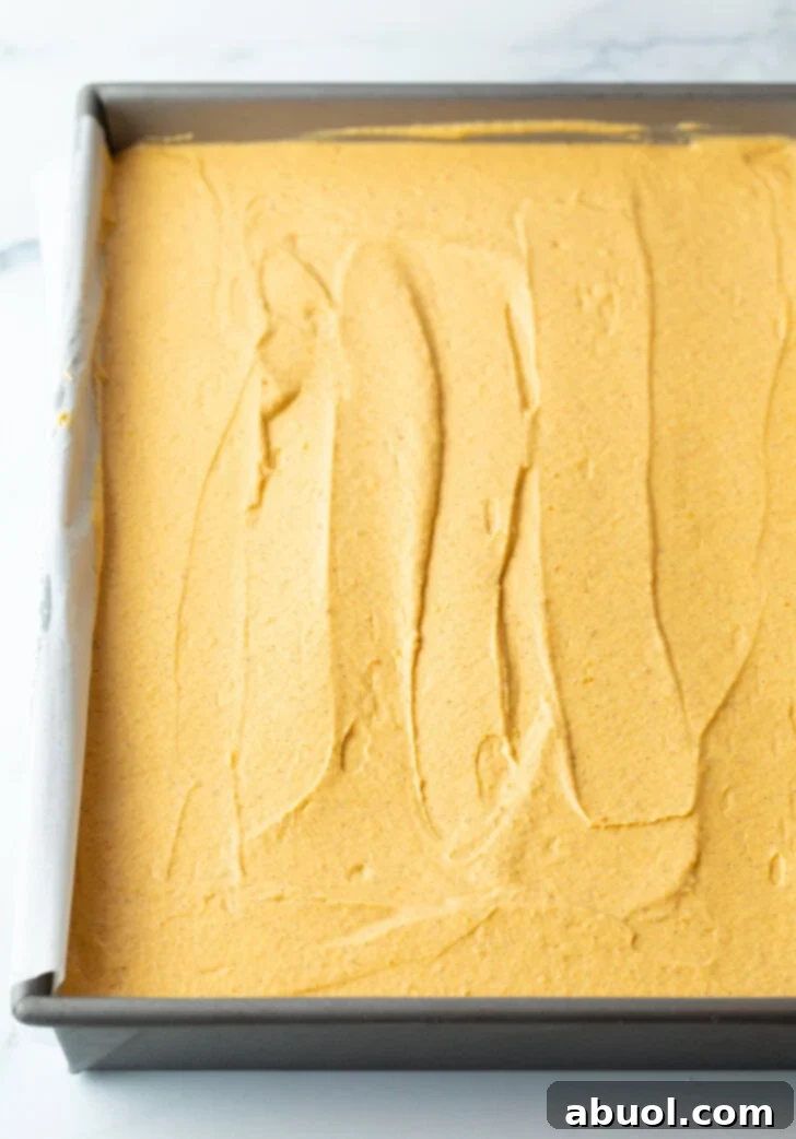 Smooth, evenly spread pumpkin cheesecake filling in a rectangle baking dish, ready for chilling.
