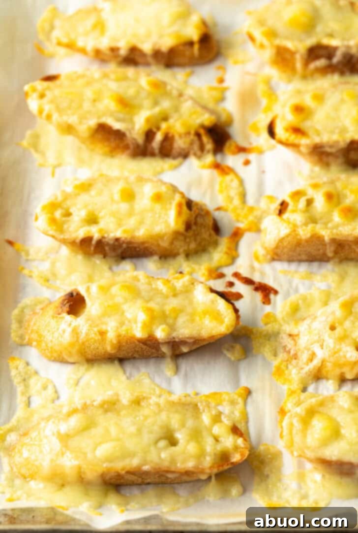 Ten slices of baguette on a baking sheet, now beautifully golden and bubbly with perfectly melted cheese, fresh from the broiler.