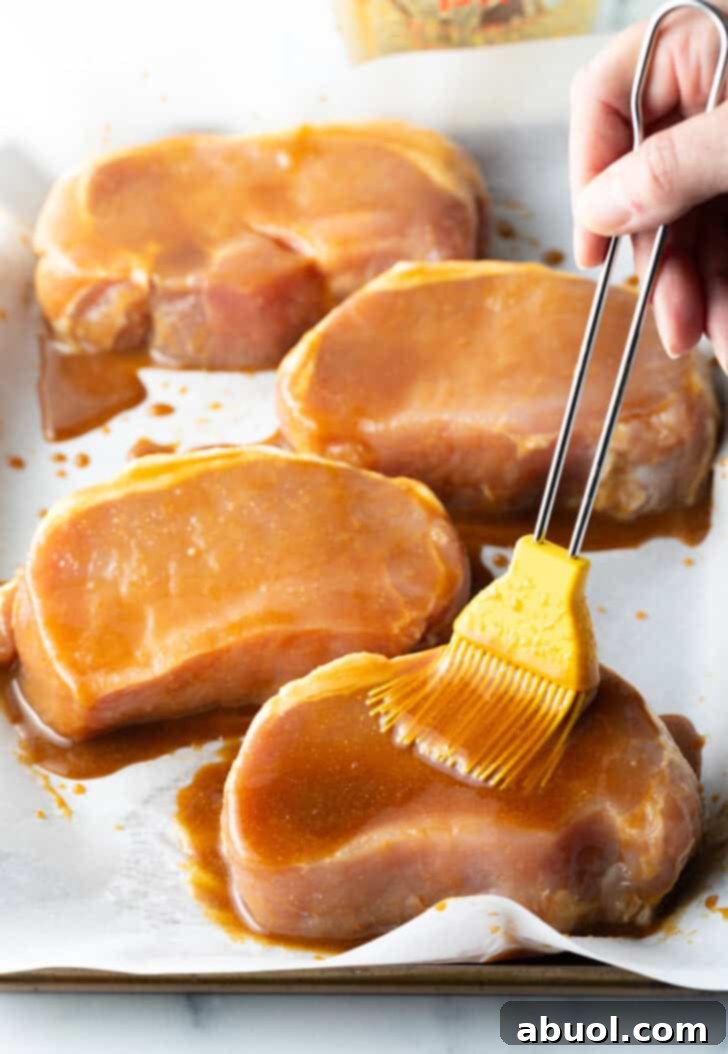 Perfectly Baked Pork Chops 7 Applying the delicious glaze: brushing it generously over raw pork chops arranged on a baking sheet.