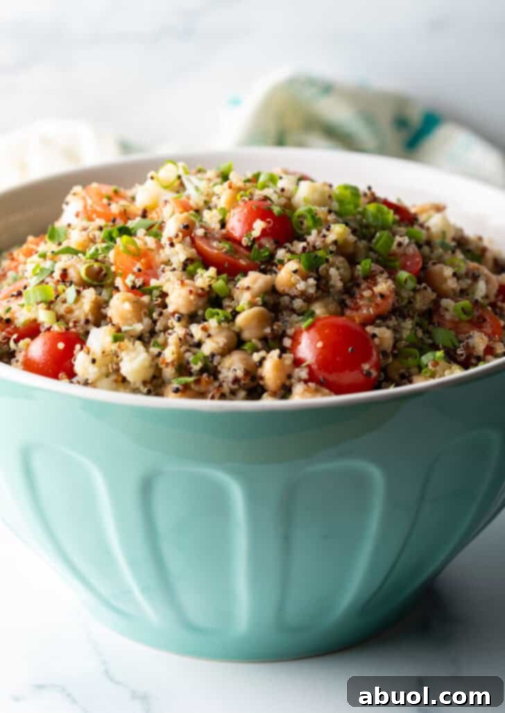Bowl of quinoa salad with cherry tomatoes, chopped fresh herbs, and chickpeas.
