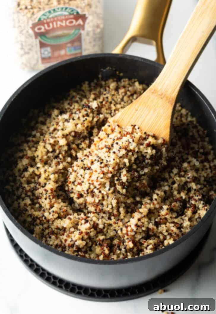 Stirring fluffy quinoa in a large black skillet with a wood spatula.