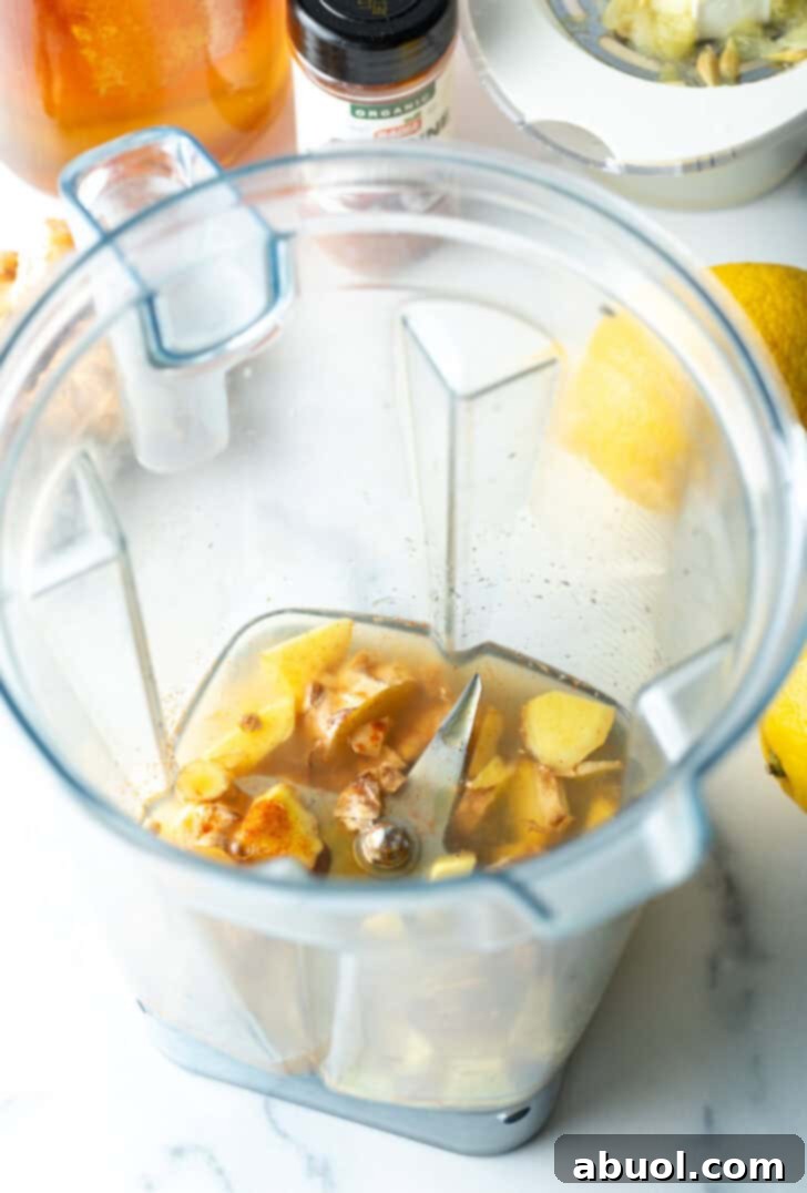 Roughly chopped ginger, lemon, and turmeric pieces ready to be processed in a food processor.