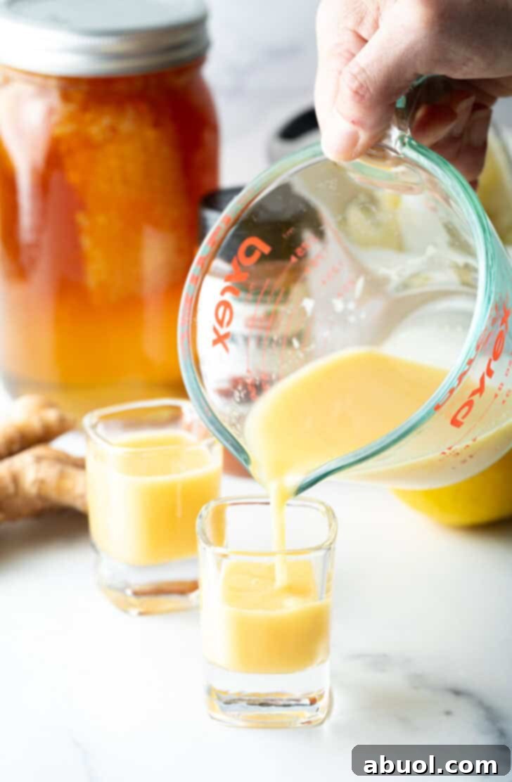 Pouring bright yellow liquid from a glass measuring pitcher into two small shot glasses, highlighting the final product.