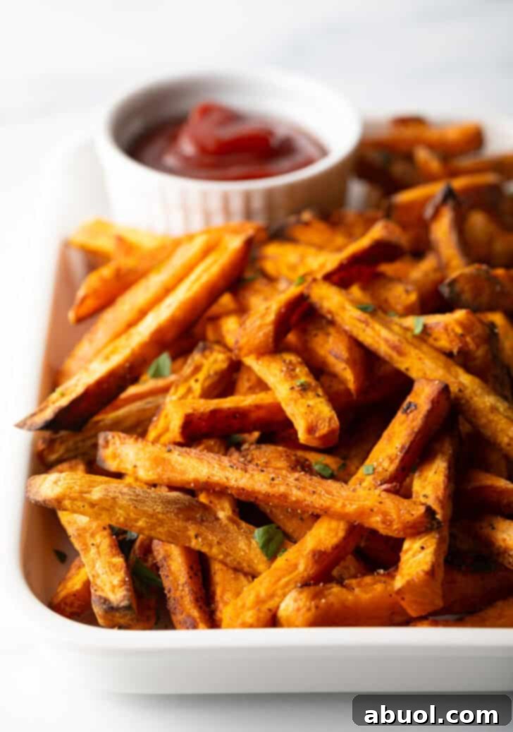 Piles of cooked sweet potatoes on a large serving pan with a white ramekin of ketchup.