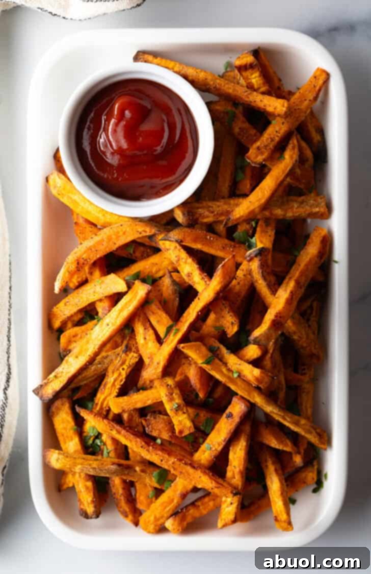 Piles of cooked air fryer sweet potatoes on a large serving pan with a white ramekin of ketchup.