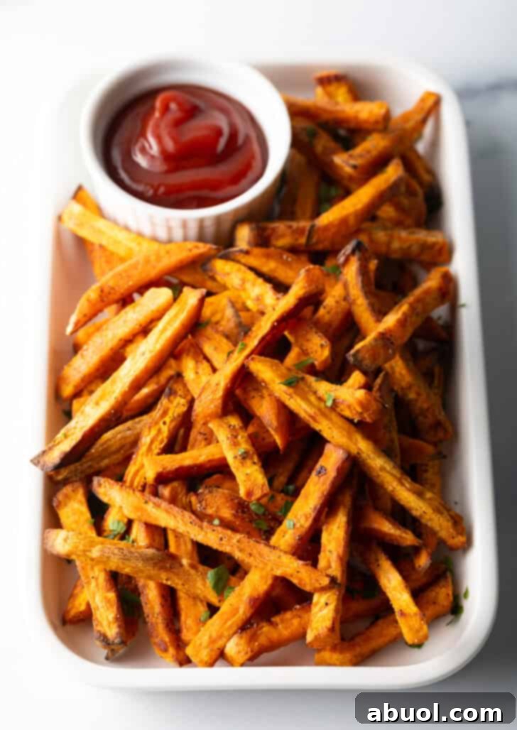 Piles of cooked air fryer or baked sweet potatoes on a large serving pan with a white ramekin of ketchup.