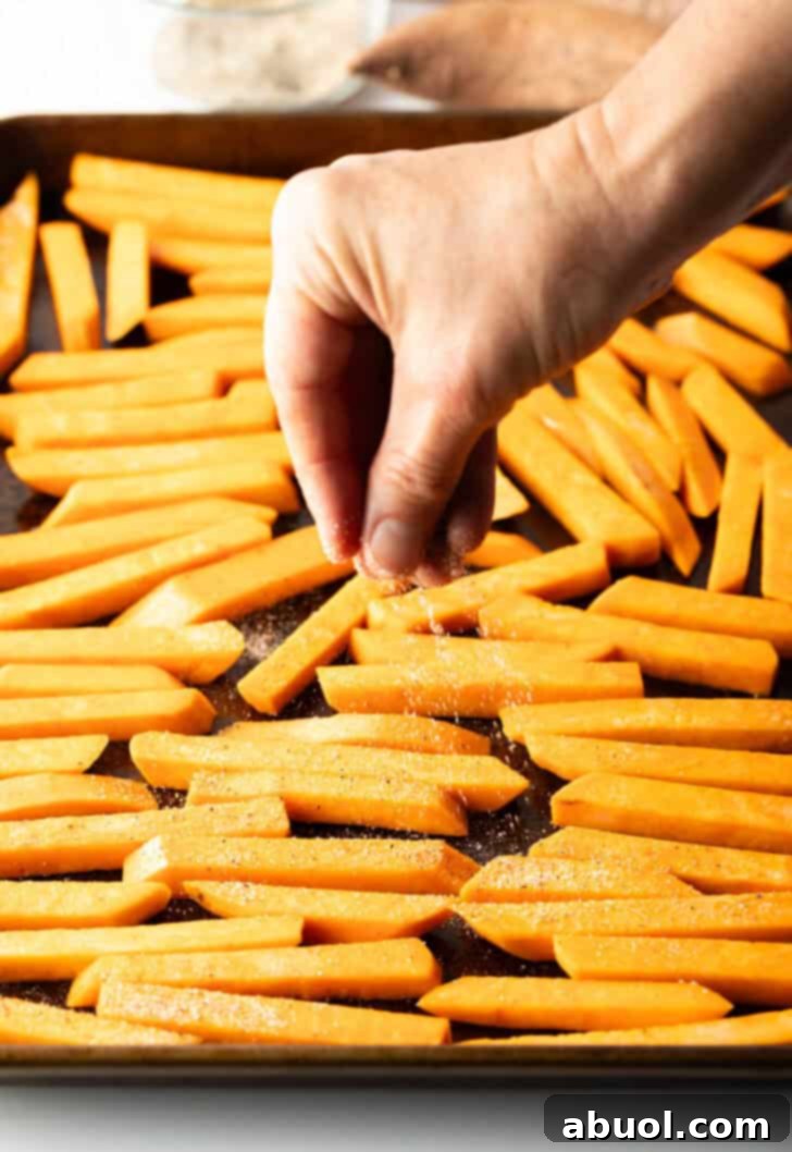 Hand placing raw slices of potatoes on a baking sheet.