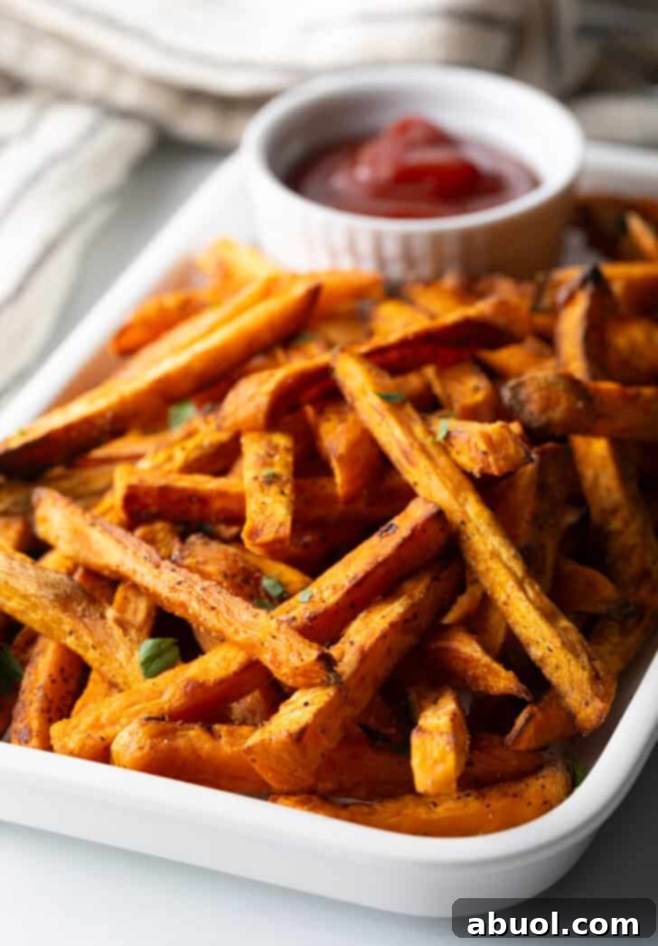 Piles of cooked baked or air fryer sweet potatoes on a large serving pan with a white ramekin of ketchup.