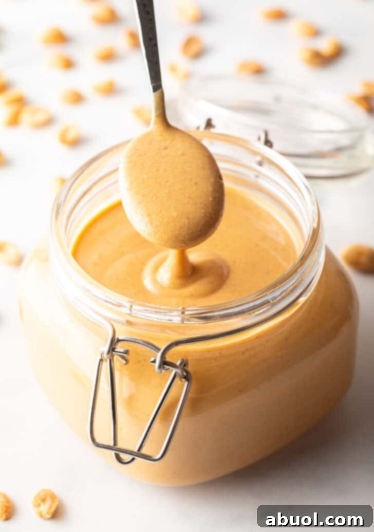 A spoon taking a scoop of creamy peanut butter from a glass jar, showcasing its smooth texture.