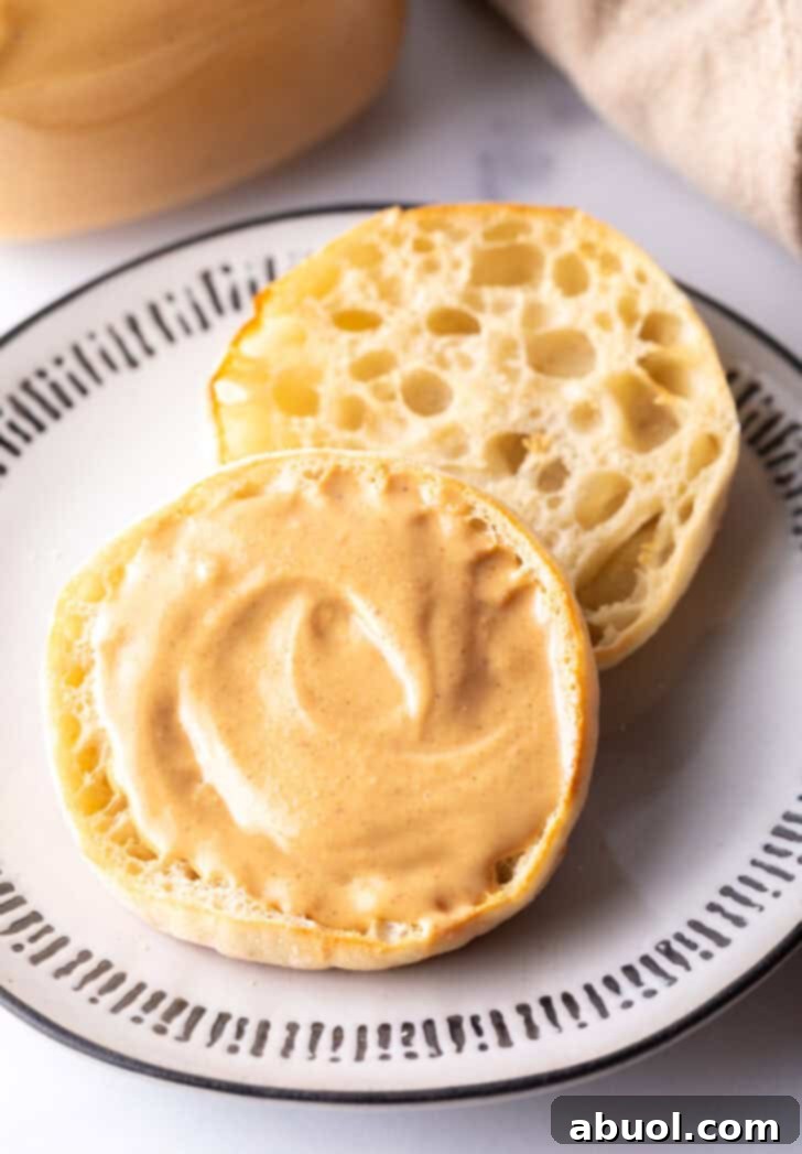 Open English muffin halves on a plate. One half is generously covered with homemade peanut butter.