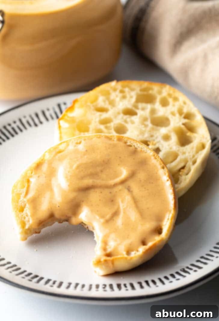 An open English muffin on a plate, with one half covered in homemade peanut butter and a bite already taken out, showcasing its delicious appeal.
