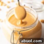 A spoon taking a scoop of peanut butter from a glass jar, showing the butter to camera.