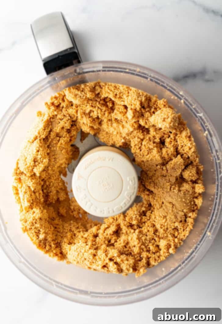 Peanuts blending further, forming a thick, sticky dough-like consistency in a food processor.