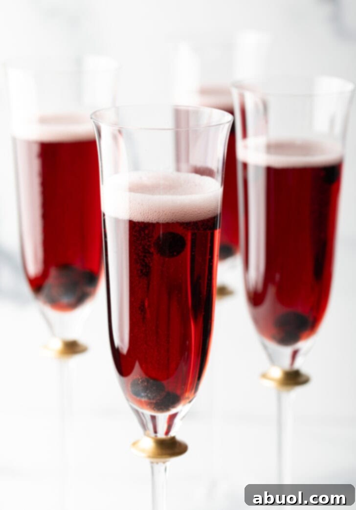 Four fluted glasses with deep red kir royale cocktail drinks.