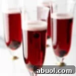 Four fluted glasses with deep red kir royale cocktail drinks.