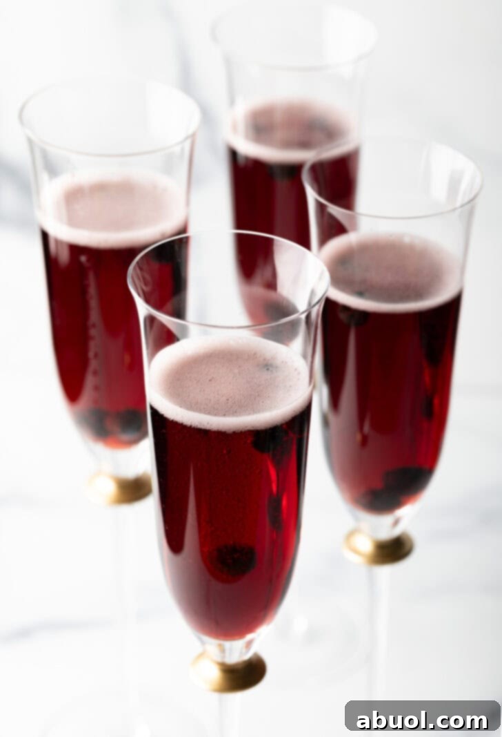 Four fluted glasses with deep red kir royale cocktail drinks.