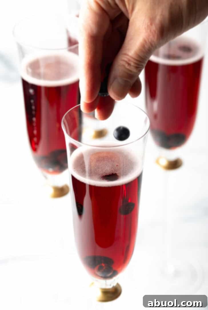 Hand sprinkling black currents into a champagne glass with red liquid.
