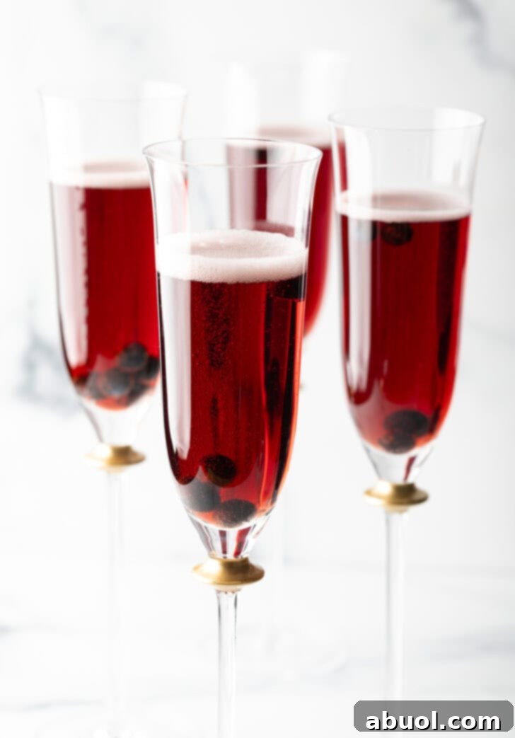 Four fluted glasses with deep red kir royale cocktail drinks.