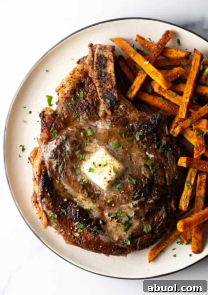 Large bone in ribeye steak on a plate with sweet potato fries.