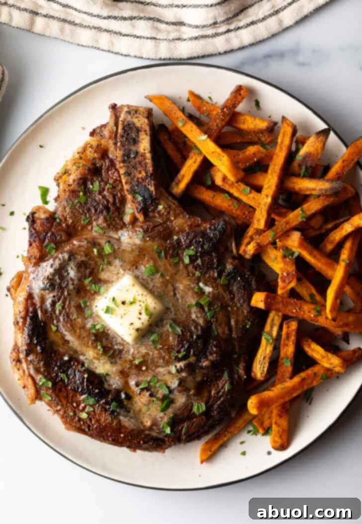 Large bone in ribeye steak on a plate with sweet potato fries.
