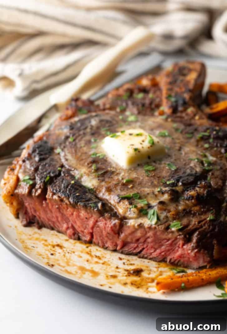 Large bone-in ribeye steak on a plate with sweet potato fries. The steak has been sliced to show the medium rare meat inside.