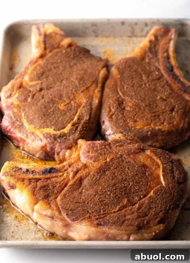 3 seasoned steaks with bones on a rimmed baking sheet.