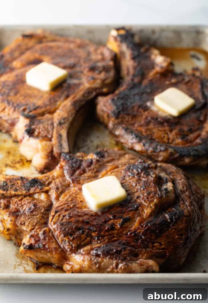 3 cooked steaks on a baking sheet, each with a pat of butter on top.
