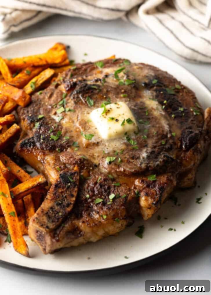 Large bone in ribeye steak on a plate with sweet potato fries.