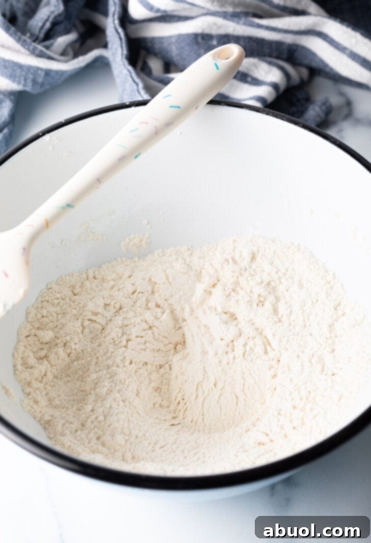 Flour and ingredients in a white bowl, with a white spatula.