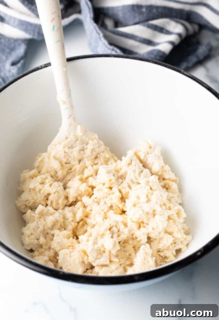 Sticky dough in a white bowl being stirred by a white spatula.